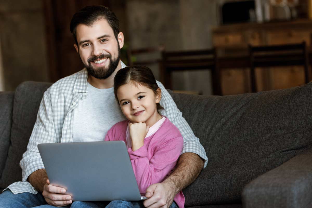 Online student working on laptop with his young daughter