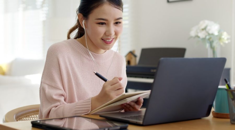 Woman taking notes while looking at a laptop