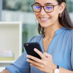 woman in blue shirt smiling at smart phone