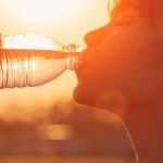 Woman drinking bottled water with sun setting in the background